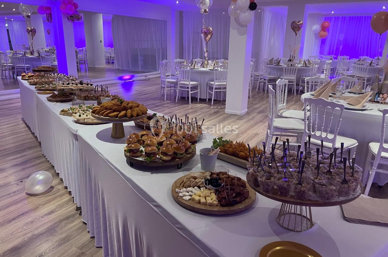 Buffet varié avec plats salés et sucrés, dans une salle décorée pour un événement festif avec tables dressées.