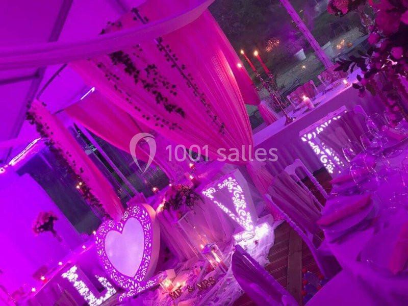 Décoration de salle de réception avec éclairage rose, rideaux, chandeliers et ornements lumineux en forme de cœur.