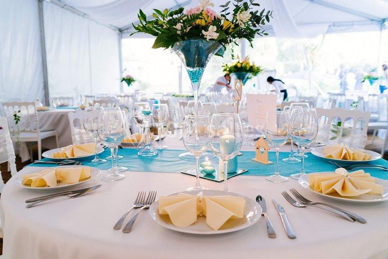 Table décorée pour un événement, avec nappes blanches, serviettes pliées, verres, couverts et centre de table floral.