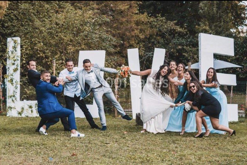 Des mariés et leurs invités posent joyeusement devant des lettres géantes formant le mot ’LOVE’ dans un jardin.