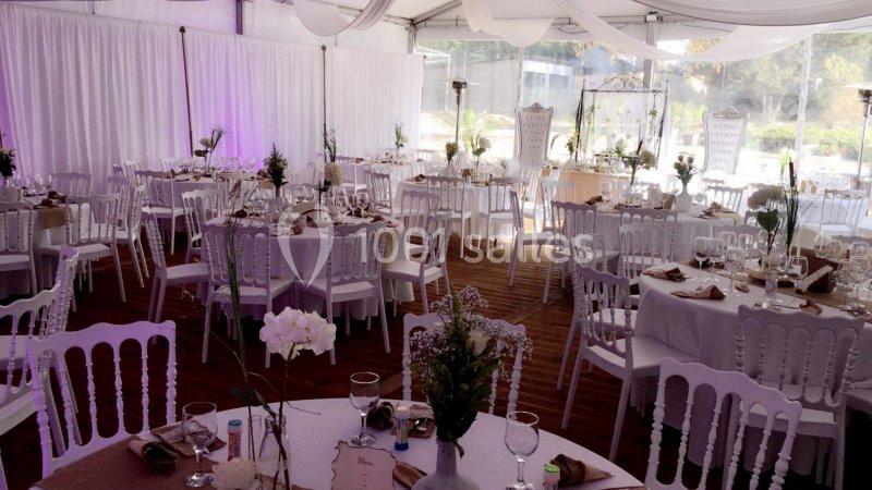 Salle de réception décorée avec des tables rondes, nappes blanches, chaises assorties et arrangements floraux.