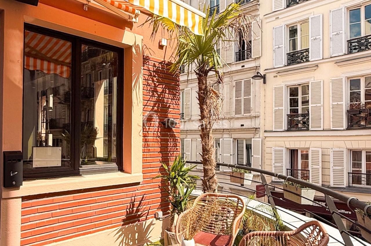 Terrasse ensoleillée avec mobilier en rotin, plantes et vue sur des immeubles parisiens aux façades claires.
