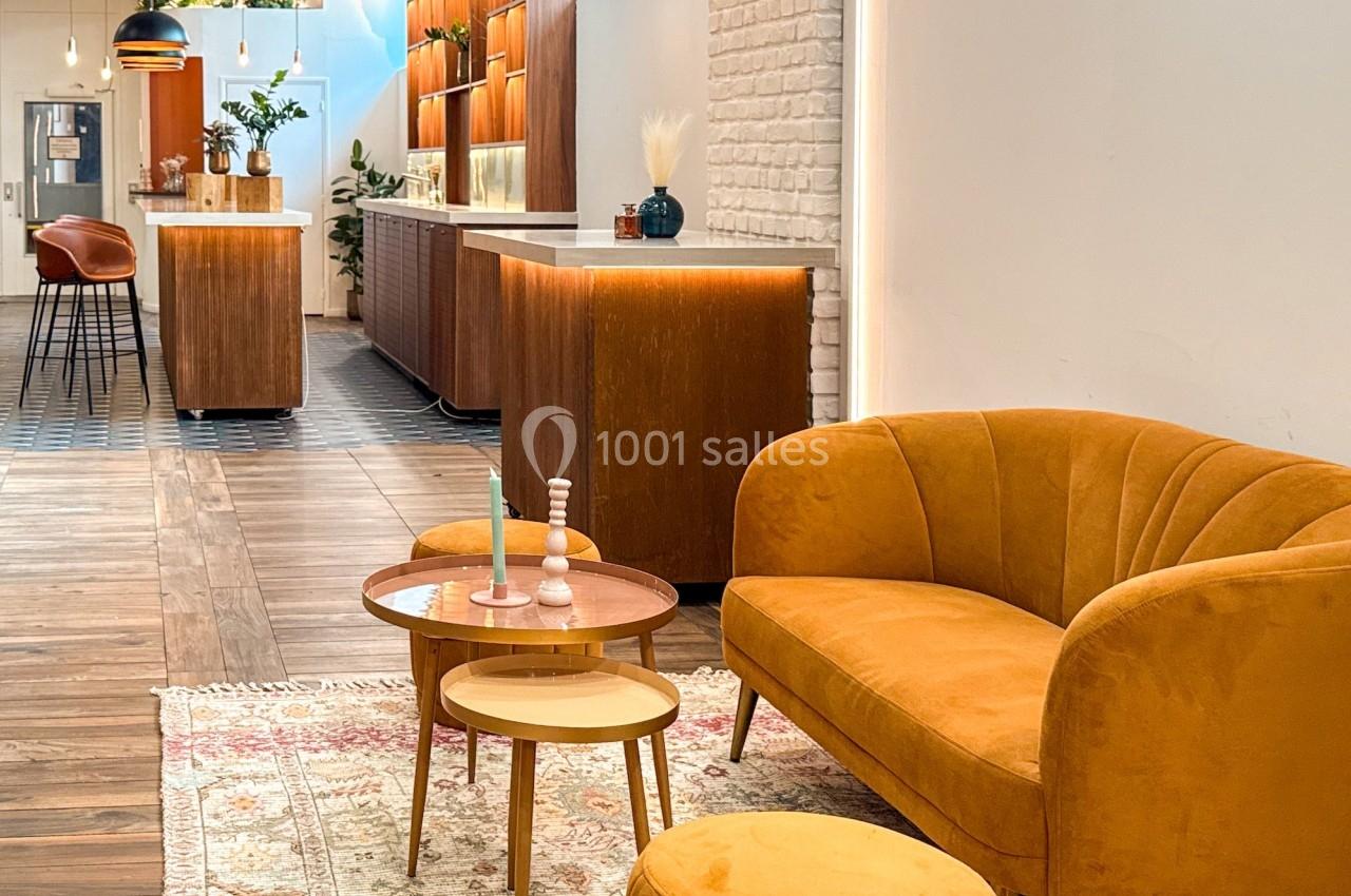 Espace intérieur chaleureux avec canapé orange, tables basses, tapis et comptoirs en bois éclairés.