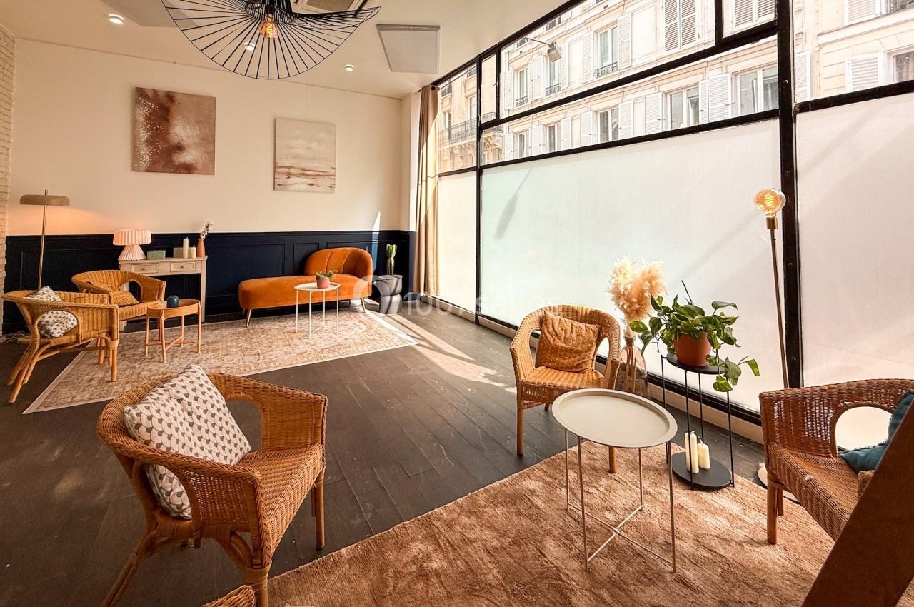 Salle lumineuse avec grandes baies vitrées, mobilier en rotin, canapé orange et décorations modernes.