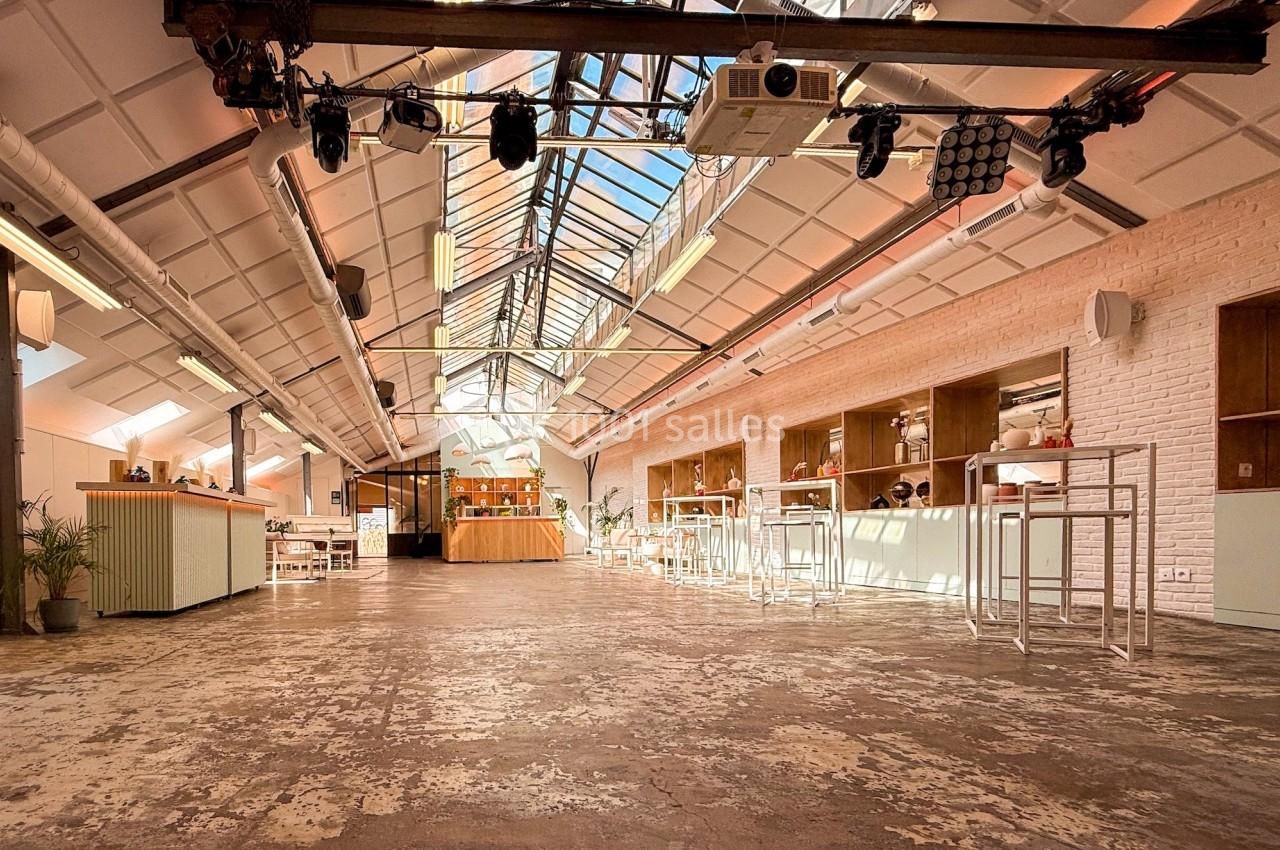 Salle lumineuse avec verrière, mobilier minimaliste et sol en béton, aménagée pour des événements ou réunions.