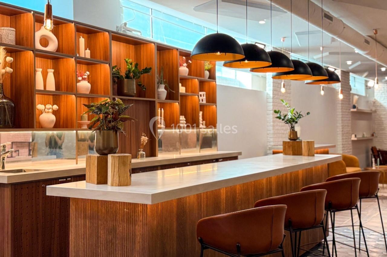 Intérieur d'un café moderne avec un comptoir en bois, des étagères décoratives et des suspensions lumineuses noires.