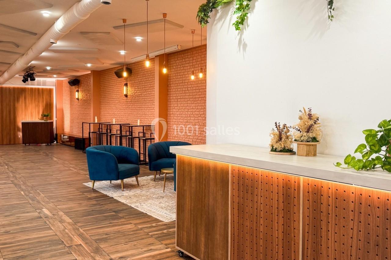 Espace intérieur moderne avec parquet, comptoir en bois, plantes décoratives et fauteuils bleus près d'un mur en briques.