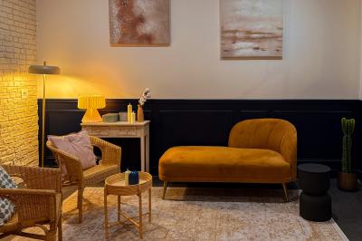 Salon chaleureux avec canapé jaune, fauteuils en rotin, table basse ronde, lampes et décorations murales abstraites.