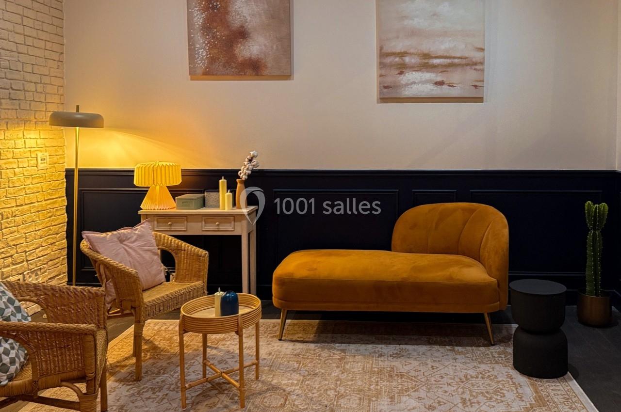 Salon chaleureux avec canapé jaune, fauteuils en rotin, table basse ronde, lampes et décorations murales abstraites.