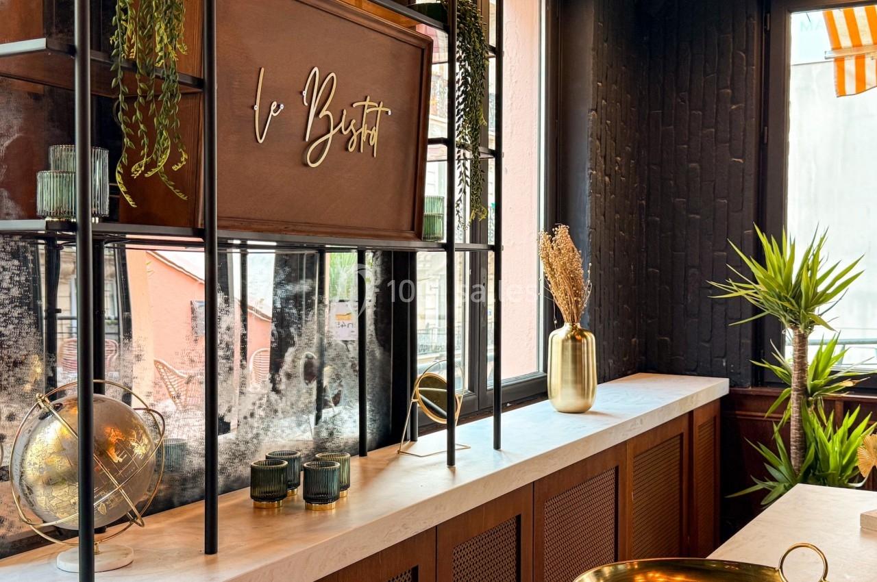 Étagère décorative avec plantes suspendues, globe terrestre, bougies et vase doré près d'une fenêtre lumineuse.