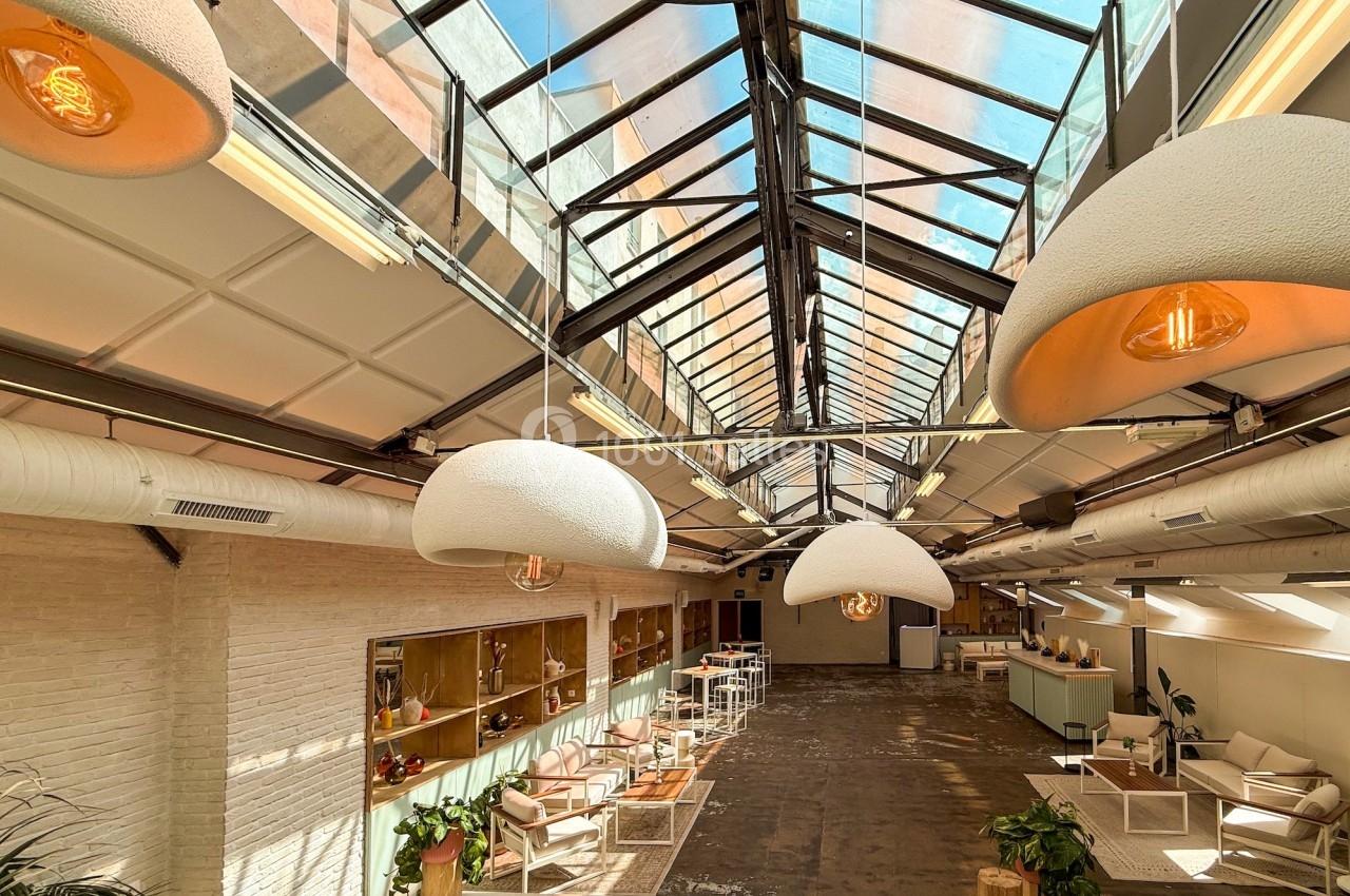 Espace lumineux avec verrière, mobilier moderne, plantes et éclairage suspendu dans un intérieur de style industriel.