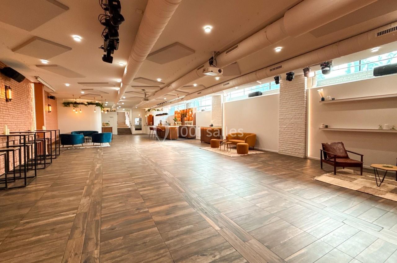 Salle lumineuse avec parquet, murs clairs, mobilier moderne et espace aménagé pour des événements ou réunions.