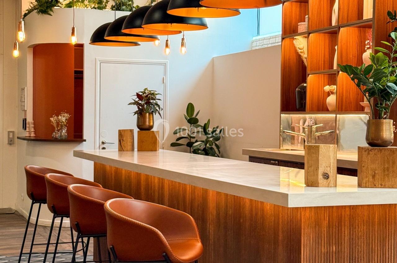 Comptoir en bois avec tabourets orange, luminaires suspendus noirs et étagères décorées dans un espace moderne et lumineux.