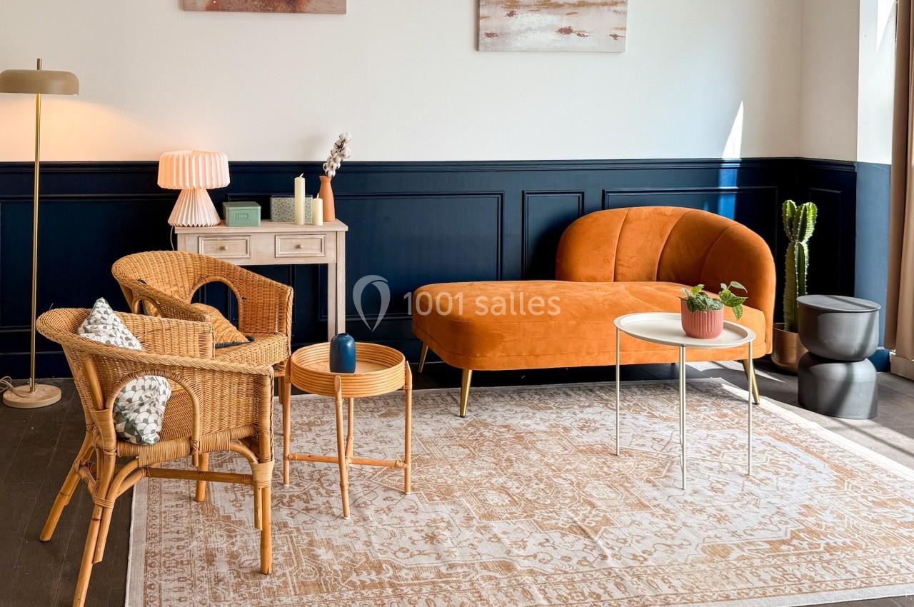 Salon lumineux avec canapé orange, fauteuils en rotin, tables basses et décoration moderne sur un tapis beige.