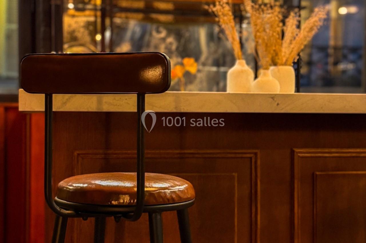 Tabouret en cuir devant un comptoir en bois, avec des vases décoratifs et un panneau lumineux en arrière-plan.