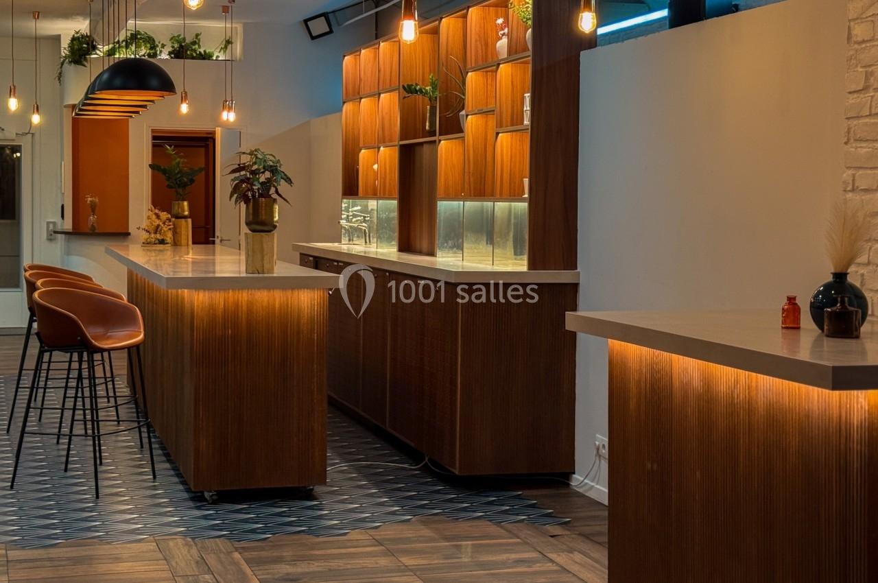 Intérieur d'un bar moderne avec comptoirs en bois, tabourets hauts, éclairage suspendu et décoration végétale.