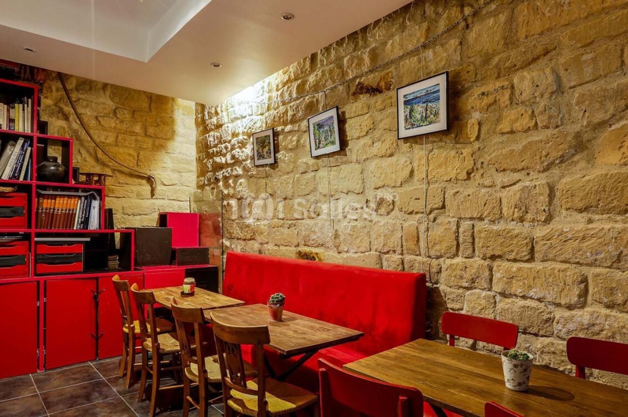 Salle avec murs en pierre, étagères rouges, tables en bois, chaises assorties et décoration murale.