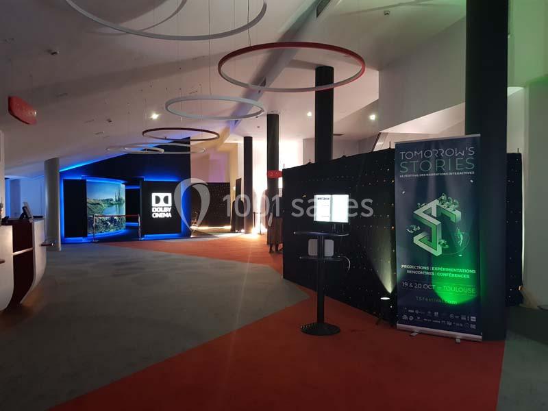 Espace intérieur moderne avec éclairage coloré, affiches promotionnelles et signalétique pour un événement.
