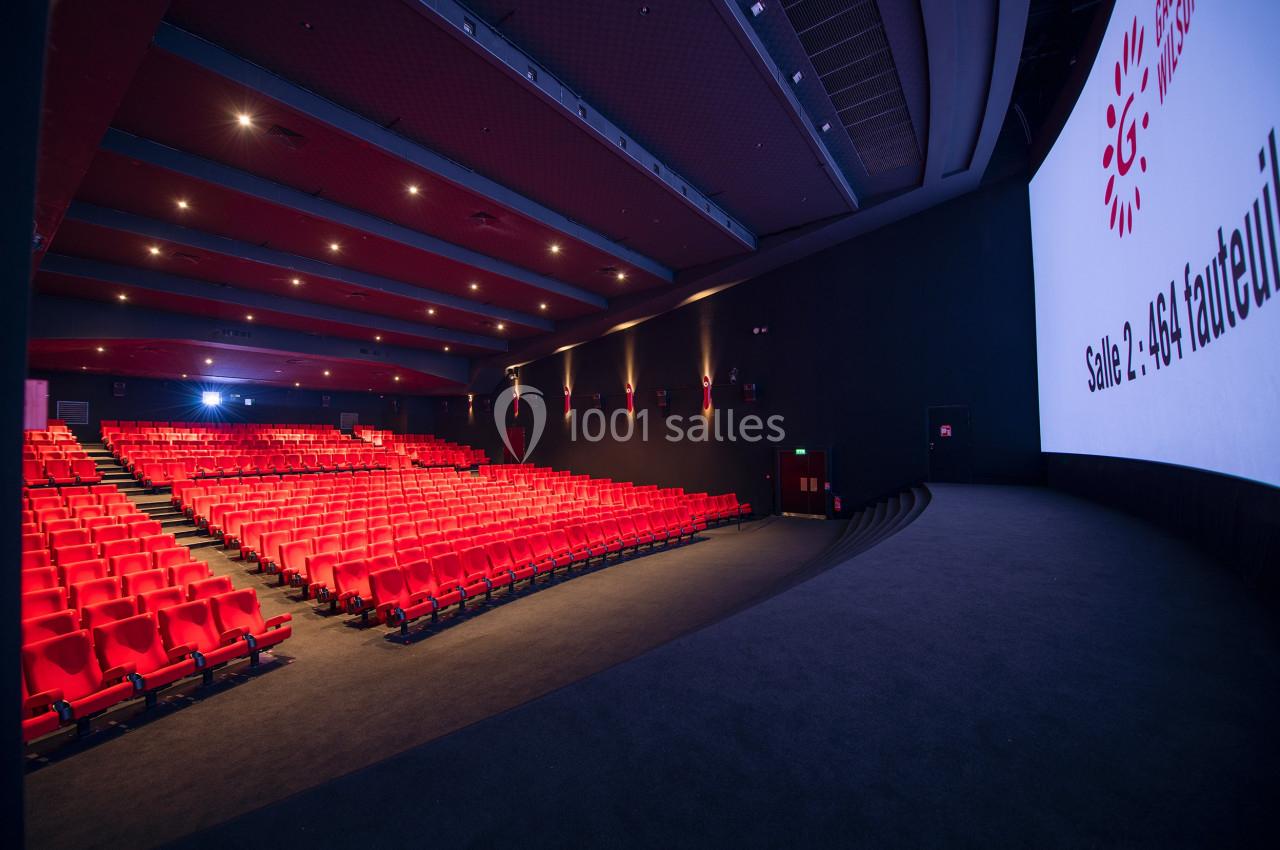 Salle de cinéma vide avec des rangées de sièges rouges, un écran géant et un éclairage tamisé.