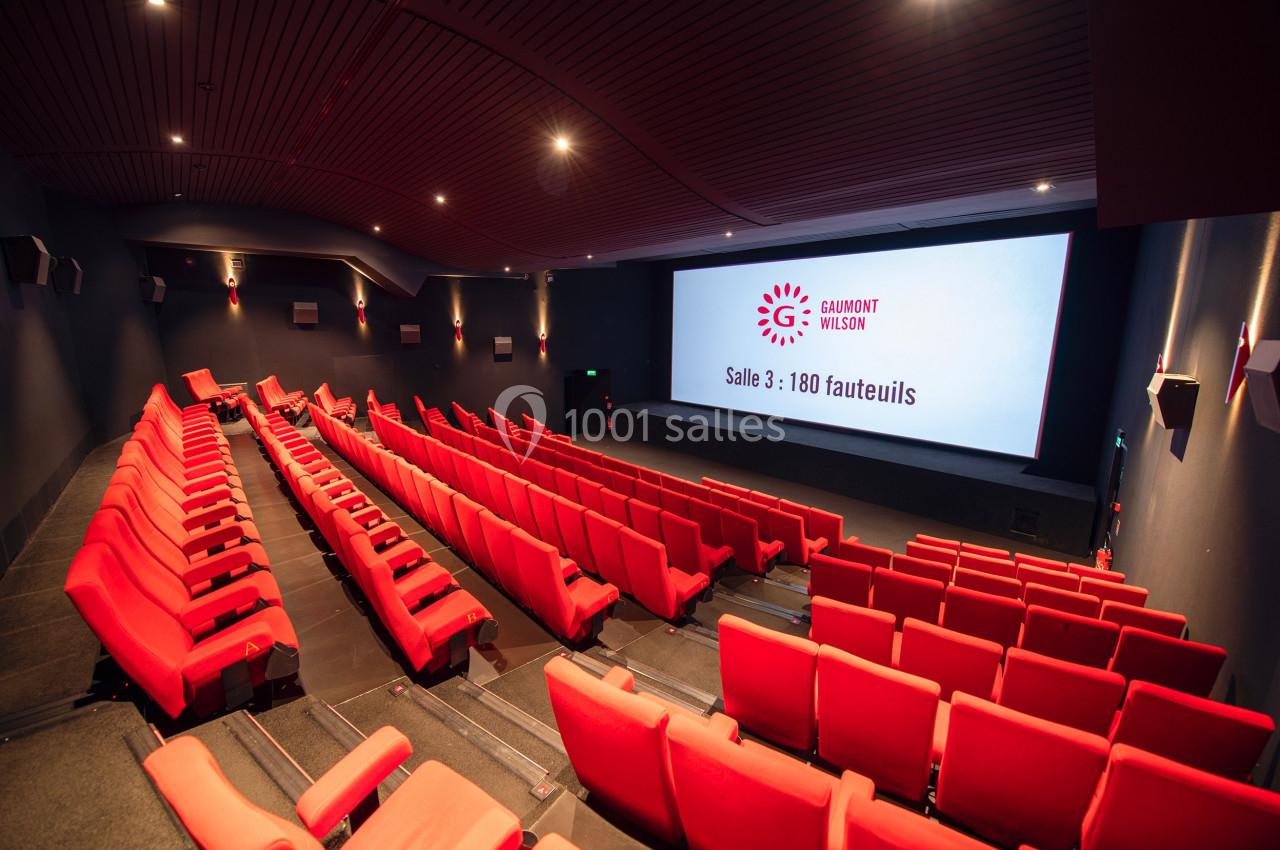 Salle de cinéma moderne avec fauteuils rouges alignés face à un grand écran affichant ’Salle 3 : 180 fauteuils’.