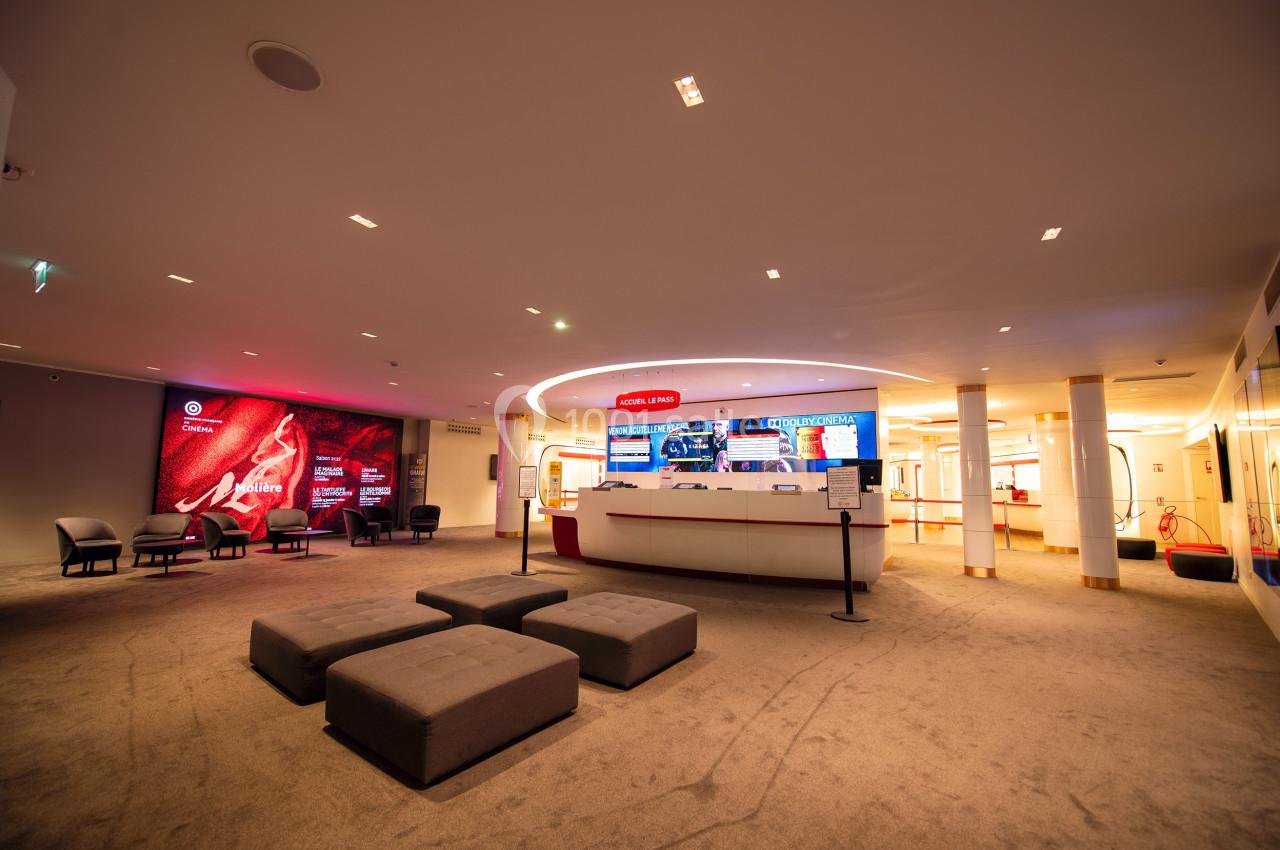 Hall d'accueil spacieux avec comptoir central, sièges, éclairage chaleureux et écrans d'affichage lumineux.