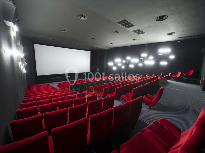 Salle de cinéma vide avec des rangées de fauteuils rouges et un grand écran blanc en fond.