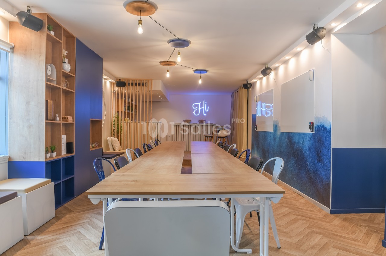Salle de réunion lumineuse avec une grande table en bois, chaises variées, décor moderne et éclairage suspendu.