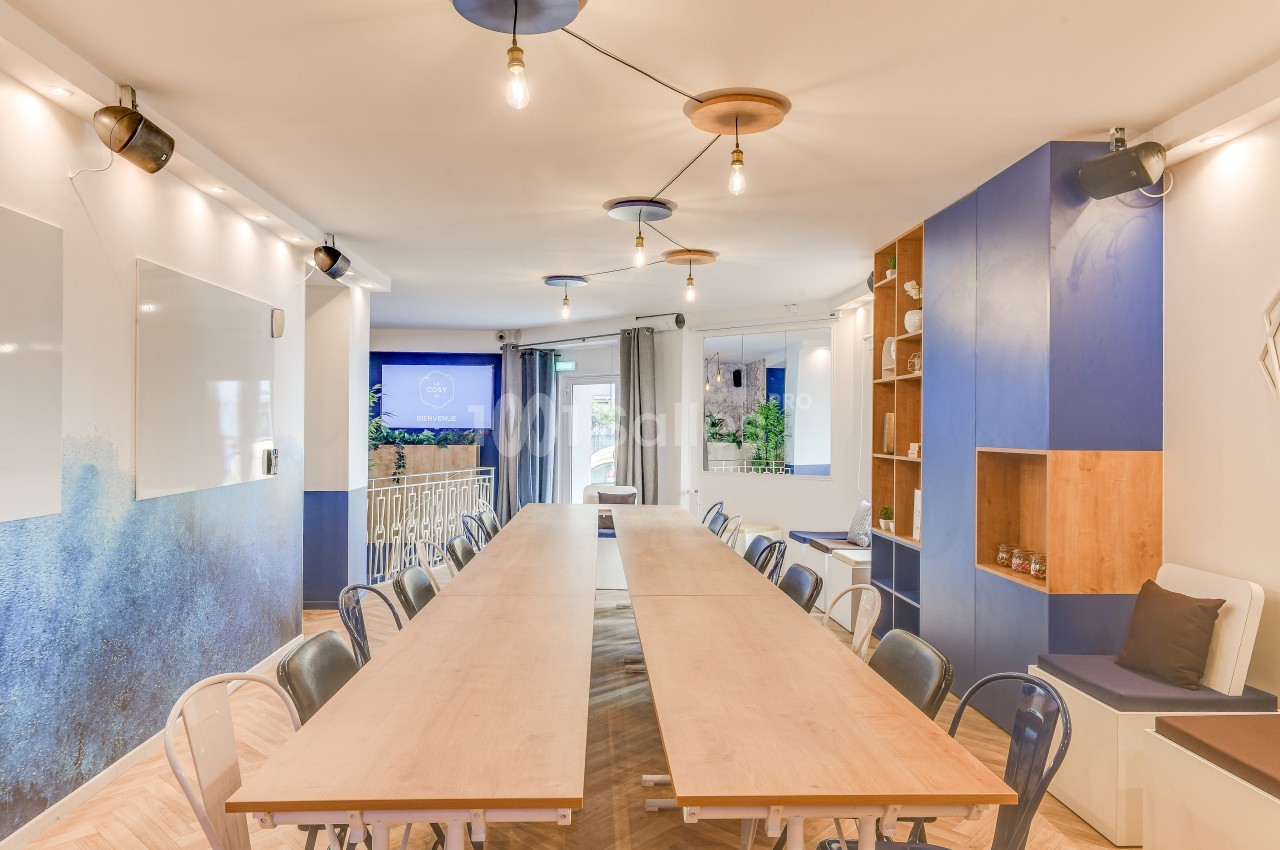 Salle de réunion lumineuse avec une grande table en bois, des chaises, des murs bleus et des étagères intégrées.