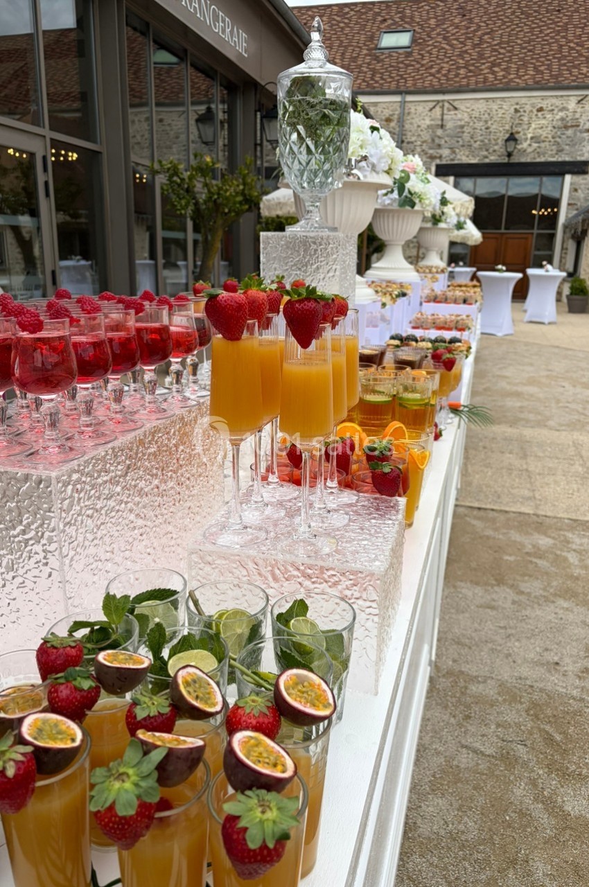 Buffet de cocktails colorés avec fruits frais, disposés sur une table en extérieur près d'un bâtiment en pierre.