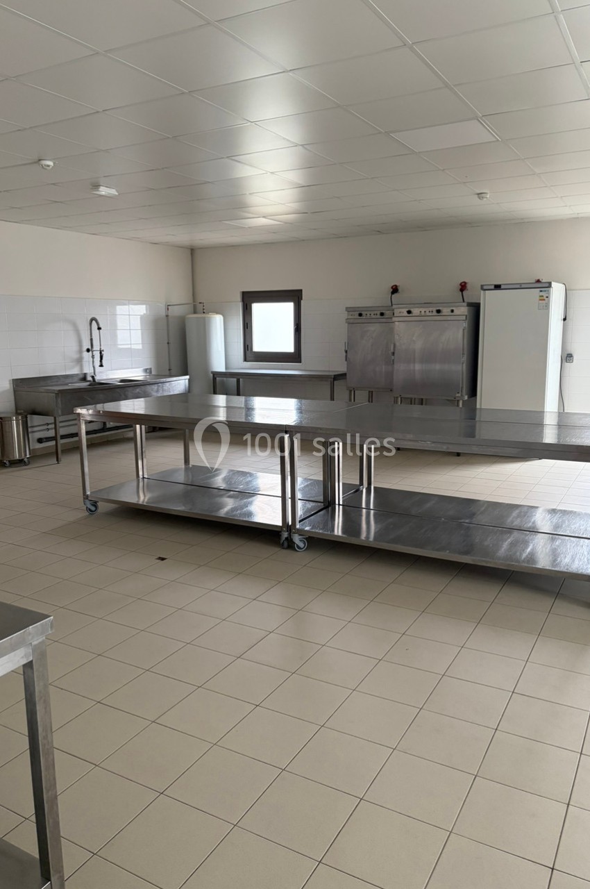 Cuisine professionnelle avec plans de travail en inox, équipements de cuisson et carrelage au sol beige.