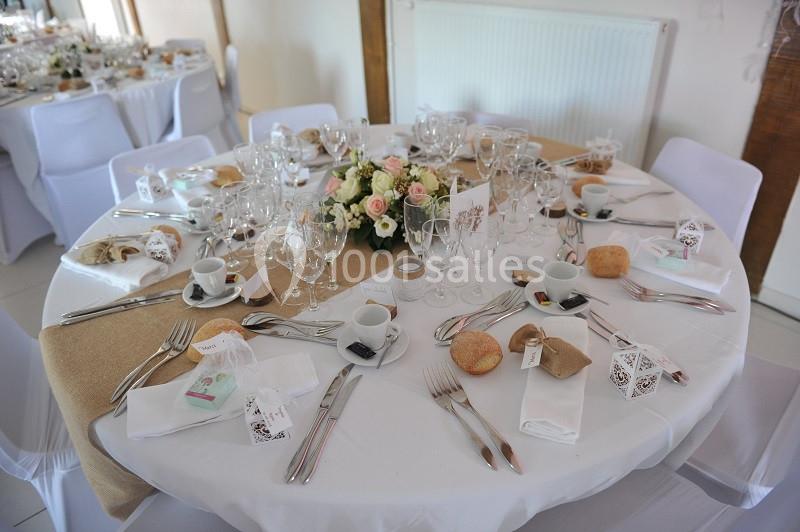 Table dressée pour un repas festif avec nappes blanches, couverts, fleurs, petits cadeaux et pains individuels.