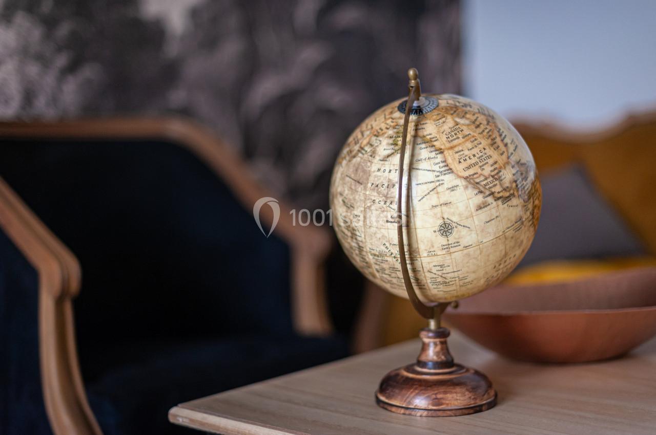 Globe terrestre ancien posé sur une table en bois, avec un fauteuil et un décor sombre en arrière-plan.