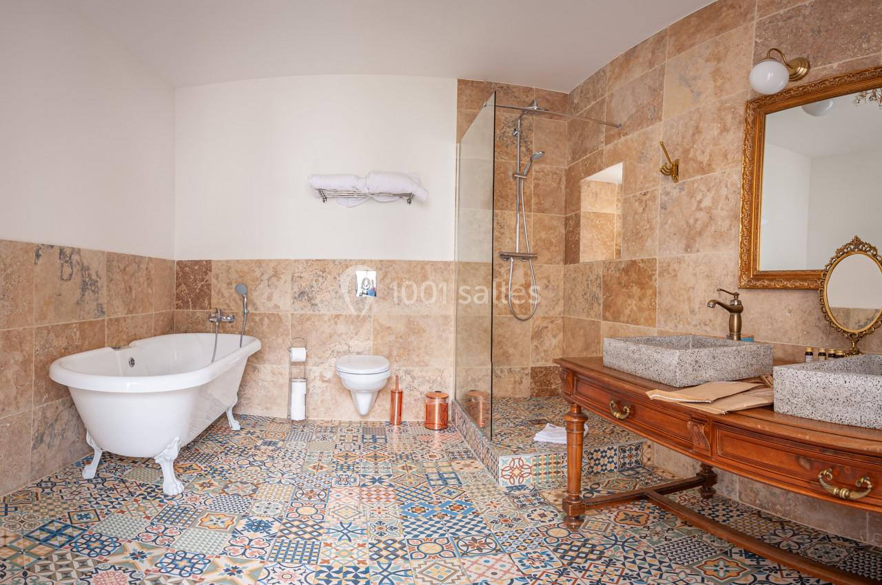 Salle de bain avec baignoire sur pieds, douche vitrée, lavabo double en pierre et carrelage à motifs colorés.
