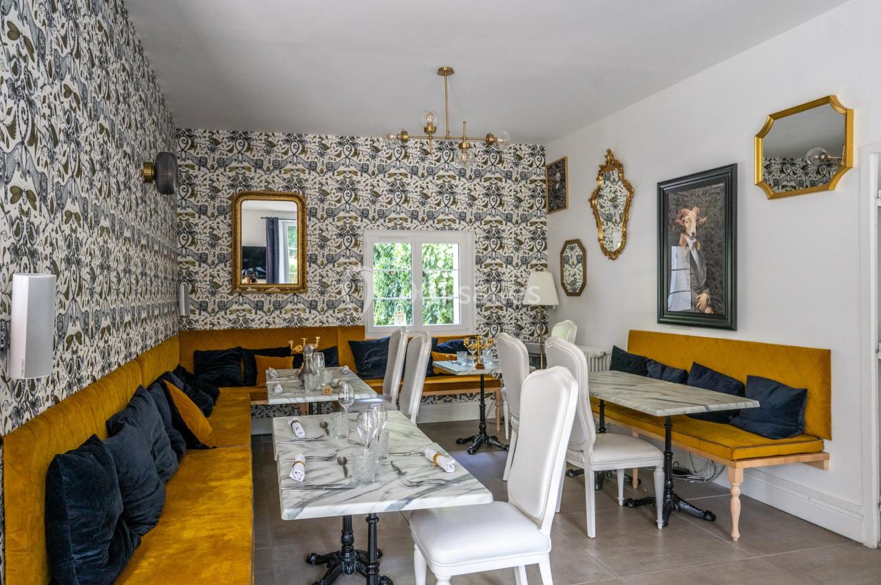 Salle à manger élégante avec banquettes moutarde, chaises blanches, tables en marbre et murs décorés de papier peint floral.