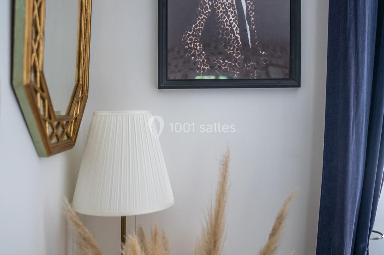 Table de chevet avec lampe, miroir doré, tableau d'un léopard en costume et bouquet de pampas dans un coin de pièce.