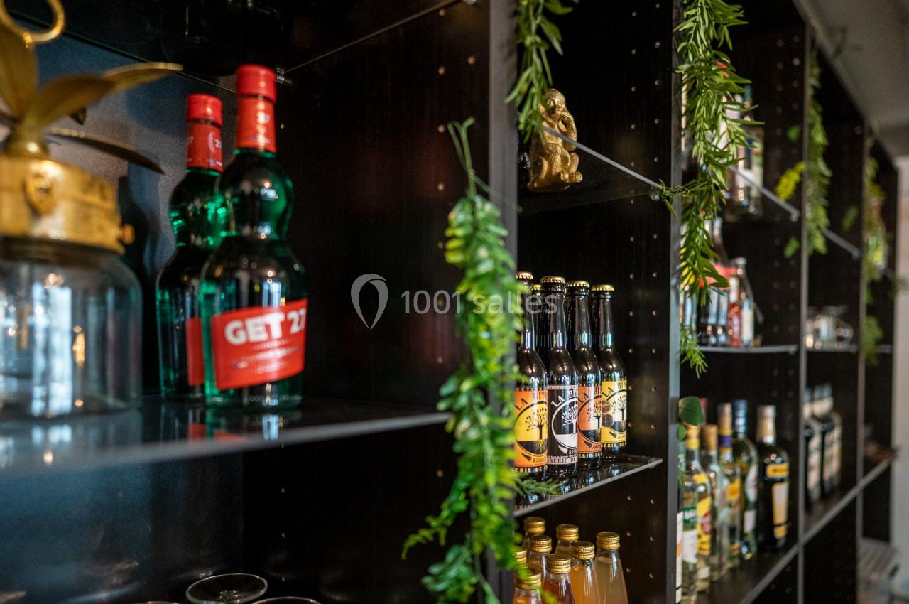 Étagères noires garnies de bouteilles d'alcool variées et décorées de plantes vertes suspendues.