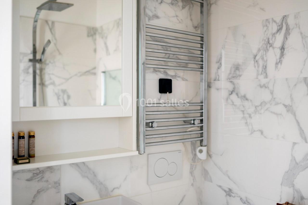 Salle de bain moderne avec lavabo, miroir, sèche-serviettes mural, douche et carrelage effet marbre.