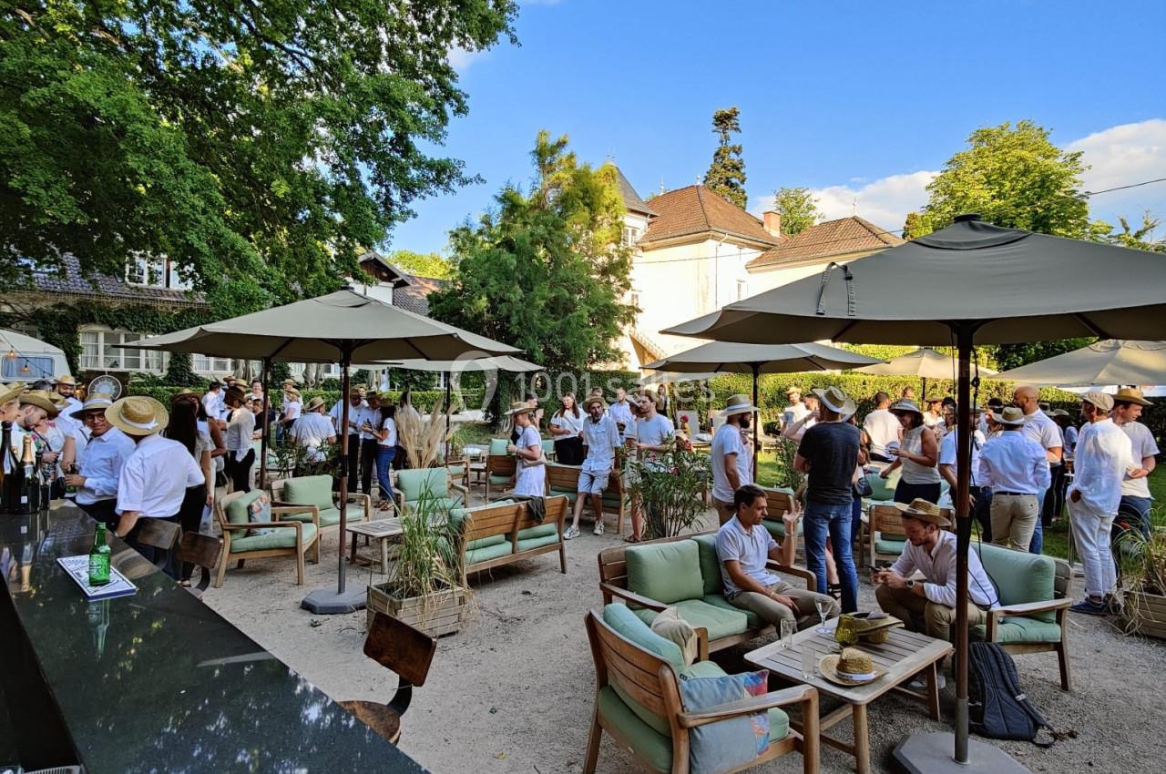 Groupe de personnes rassemblées dans un jardin avec des parasols, des tables et des chaises, par une journée ensoleillée.