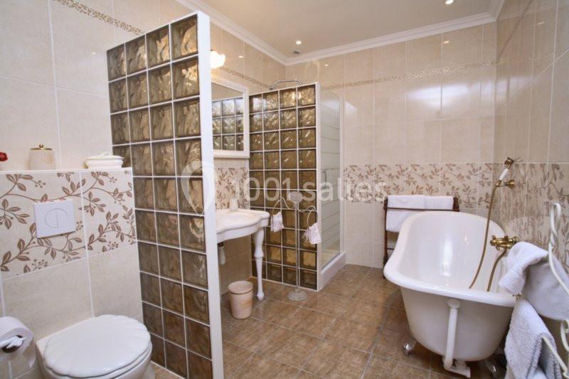 Salle de bain avec baignoire sur pieds, douche vitrée, lavabo, toilettes et carrelage beige décoré de motifs floraux.