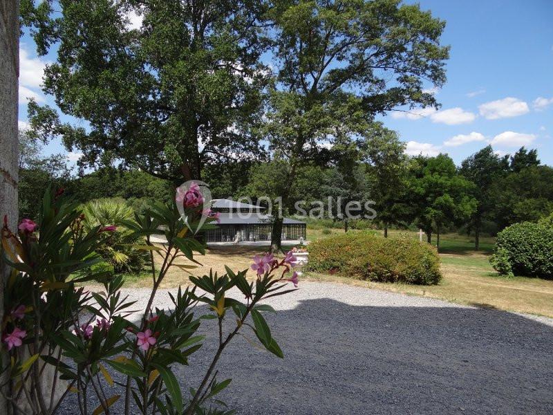 Jardin arboré avec des lauriers roses au premier plan, une terrasse et une pelouse sous un ciel bleu.