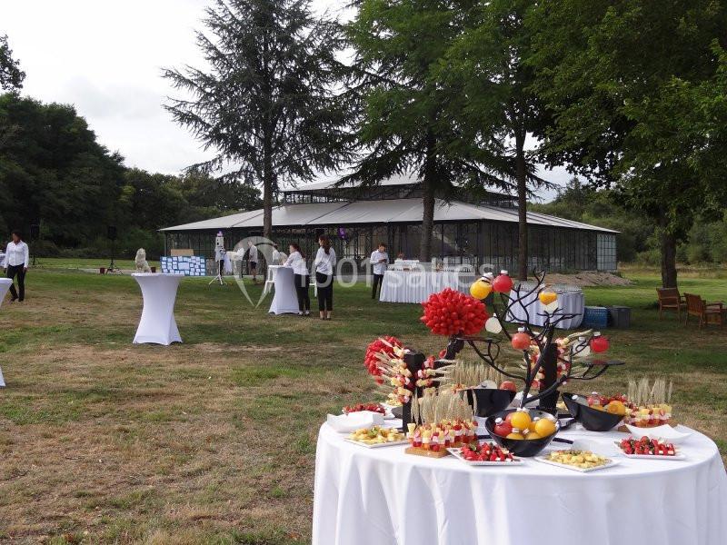 Tables dressées avec des amuse-bouches et décorations dans un jardin, avec un bâtiment vitré en arrière-plan.