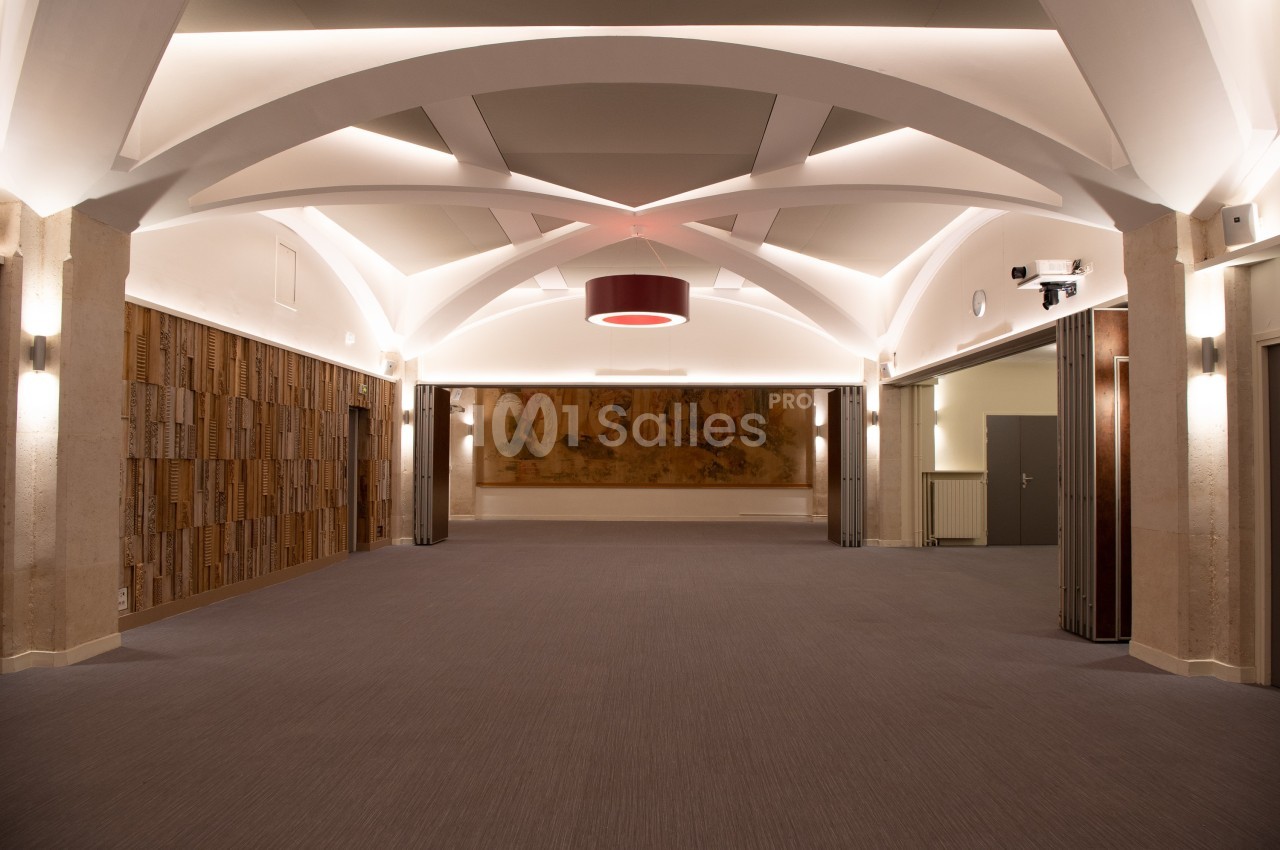 Salle vide avec plafond voûté, éclairage moderne, murs en bois et fresque murale au fond.