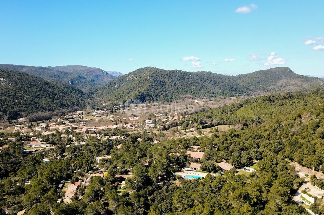 Vue aérienne d'un village entouré de collines boisées sous un ciel bleu dégagé.