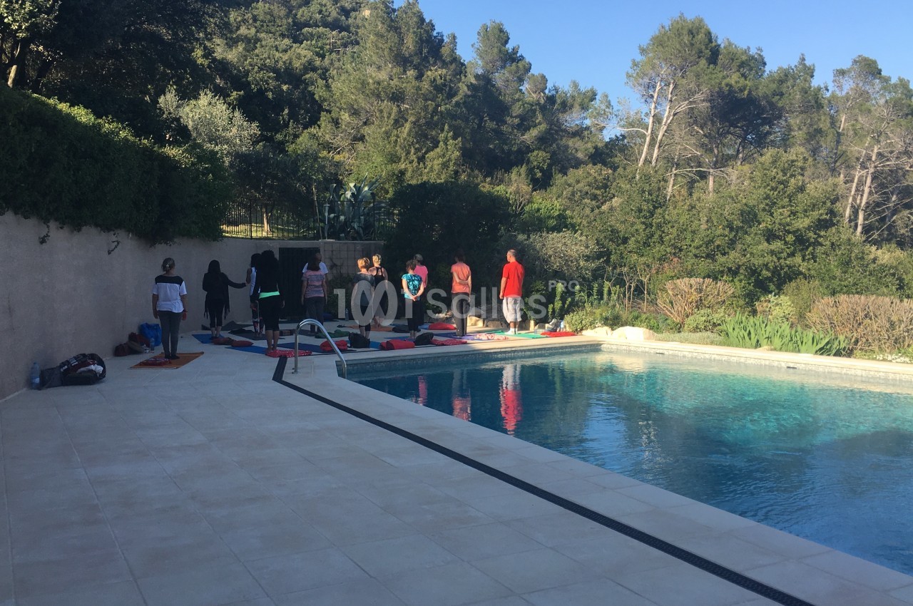 Un groupe de personnes pratique des exercices en plein air près d'une piscine entourée de végétation.