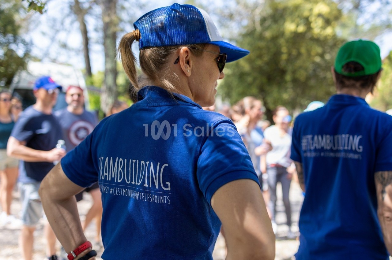 Une femme en tenue bleue avec une casquette participe à une activité de groupe en extérieur, entourée de personnes.