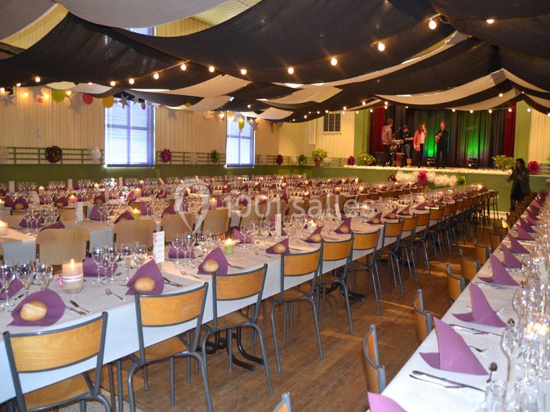 Salle décorée pour un banquet avec de longues tables dressées, nappes blanches et serviettes violettes.