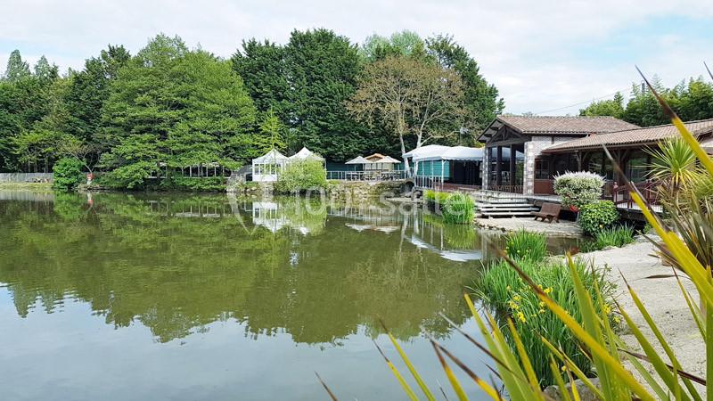 Plan d'eau entouré de végétation, avec des bâtiments en bois et des structures légères en arrière-plan.