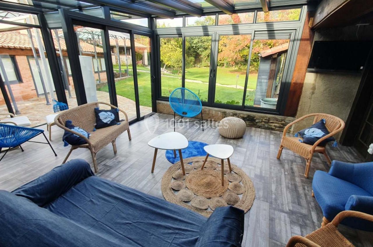 Salon lumineux avec mobilier en rotin et vue sur un jardin verdoyant à travers de grandes baies vitrées.