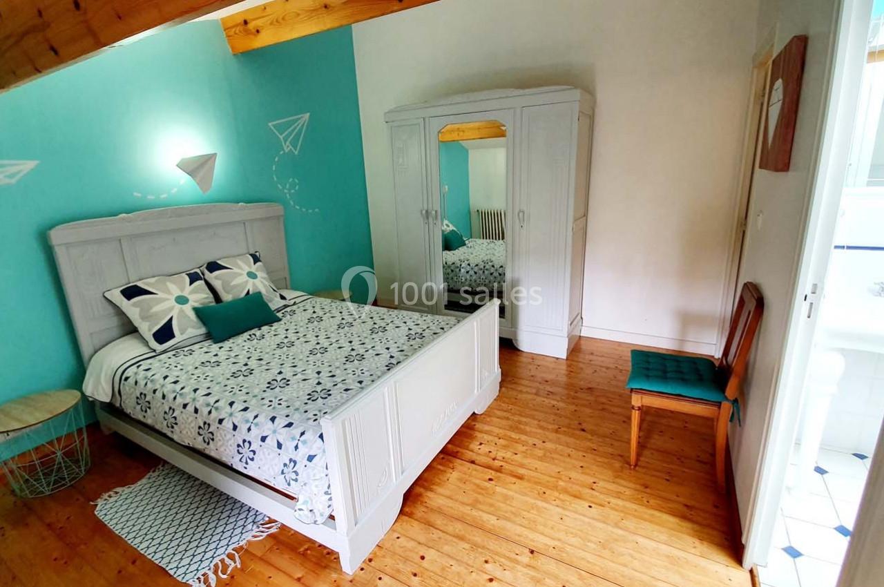 Chambre lumineuse avec lit double, armoire blanche, murs turquoise et parquet en bois clair.