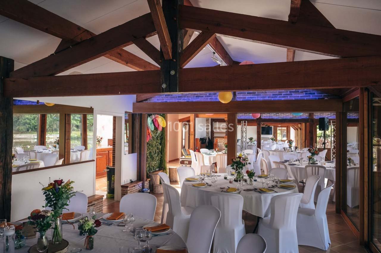 Salle de réception lumineuse avec des tables rondes dressées, des chaises blanches et une décoration colorée.